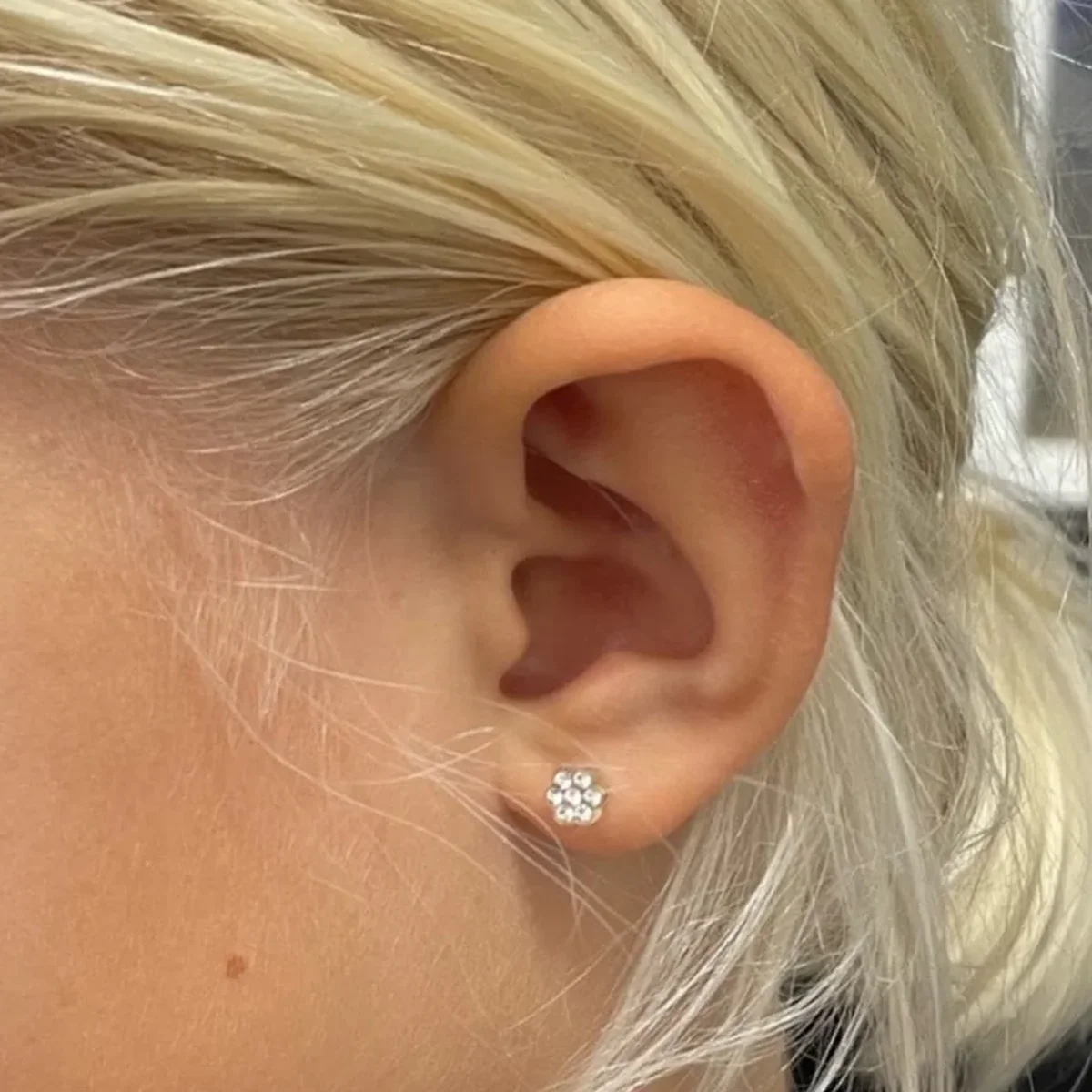 Detail ucha s květinovou kamínkovou náušnicí po nastřelení